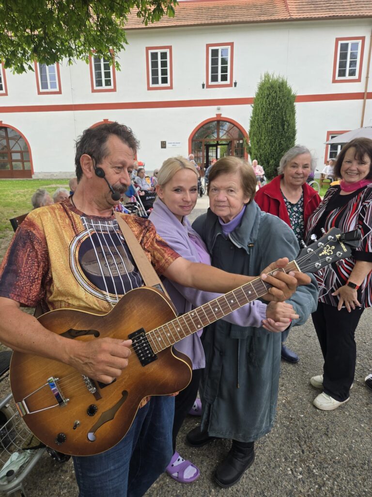 Pavel Justich hraje na kytaru a v pozadí tančí čtyři osoby