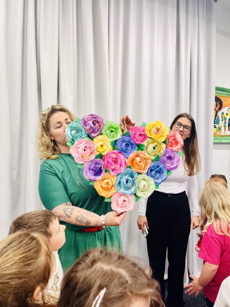 Paní učitelky ze školky ukazují klientům velké papírové srdce, které s dětmi vyrobili pro klienty