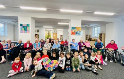 Děti z mateřské školy a klienti pózukjí na společné fotografii