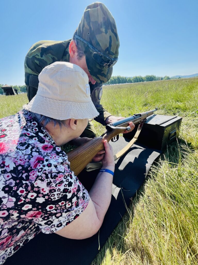 Klientka leží na zemi a míří střelnou zbraní na cíl