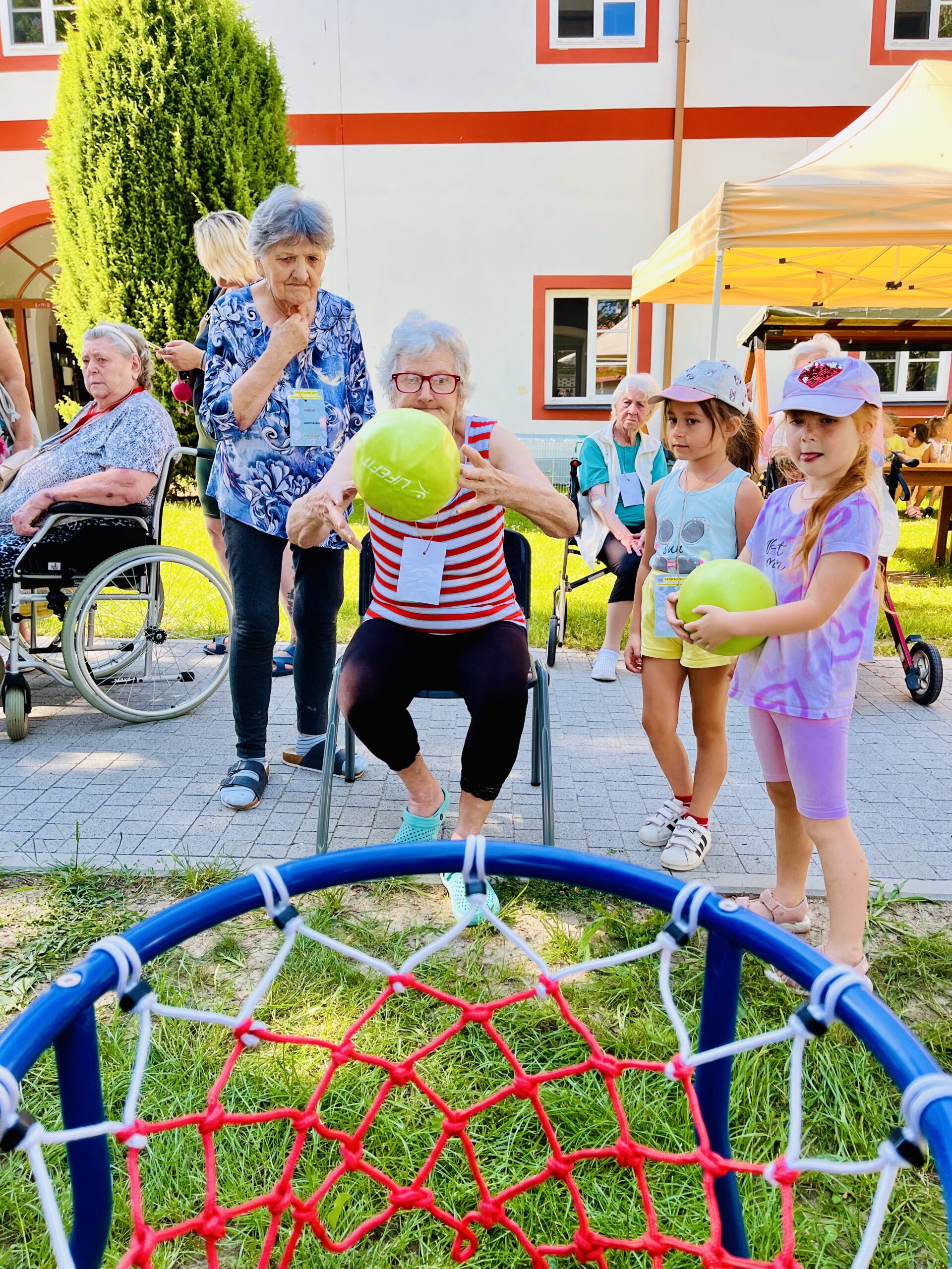 Klientka hází na koš, v pozadí děti z MŠ Mirotice a další klientka