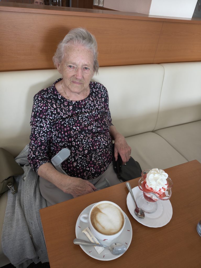 Klientka sedí v cukrárně a před sebou má pohár - jahody se šlehačkou a café latté